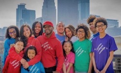 Family of 12 in red, blue, green, and purple shirts with a city skyline in background